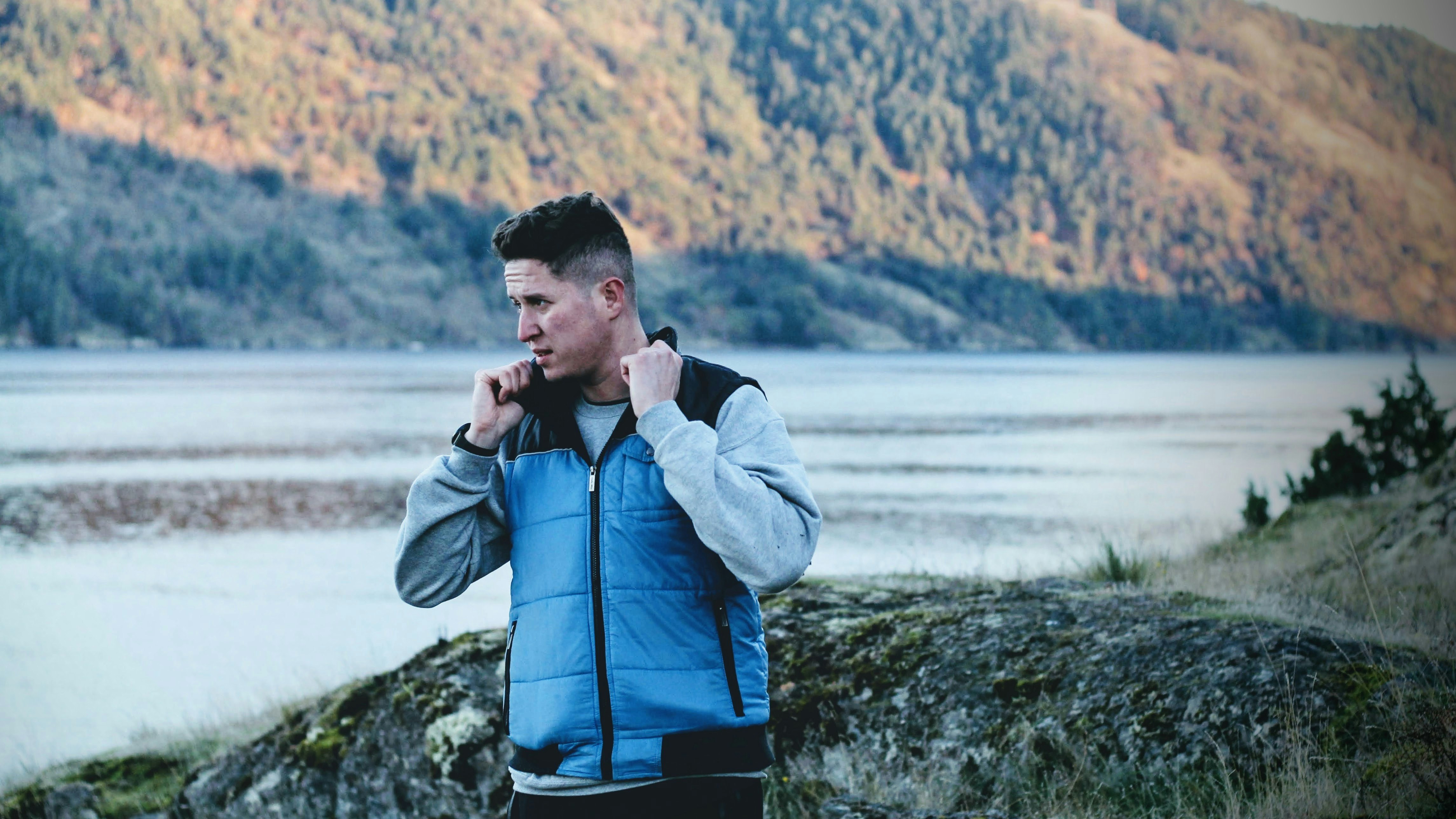 man in blue zip up jacket standing near lake during daytime